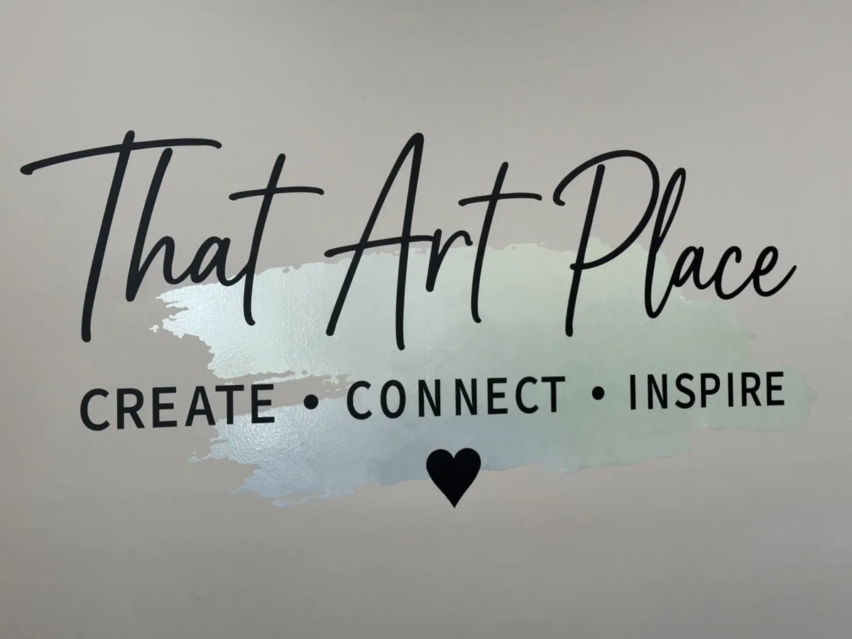 That Art Place script logo with Create, Connect, Inspire and a heart over a pale blue watercolor swash, a vinyl wall graphic on a grey interior wall