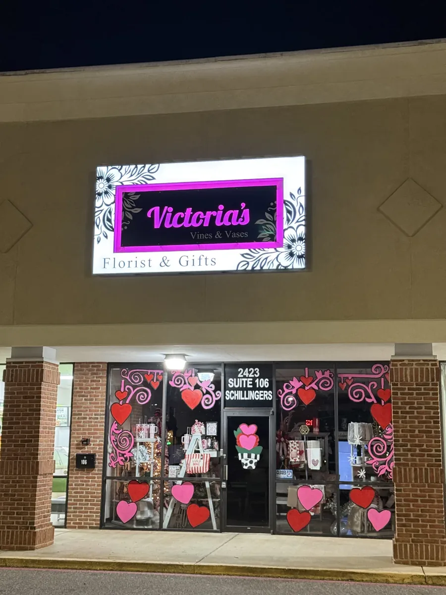 Victoria's Vines and Vases at dusk, its lit sign above windows covered in pink and red heart and swirl decals