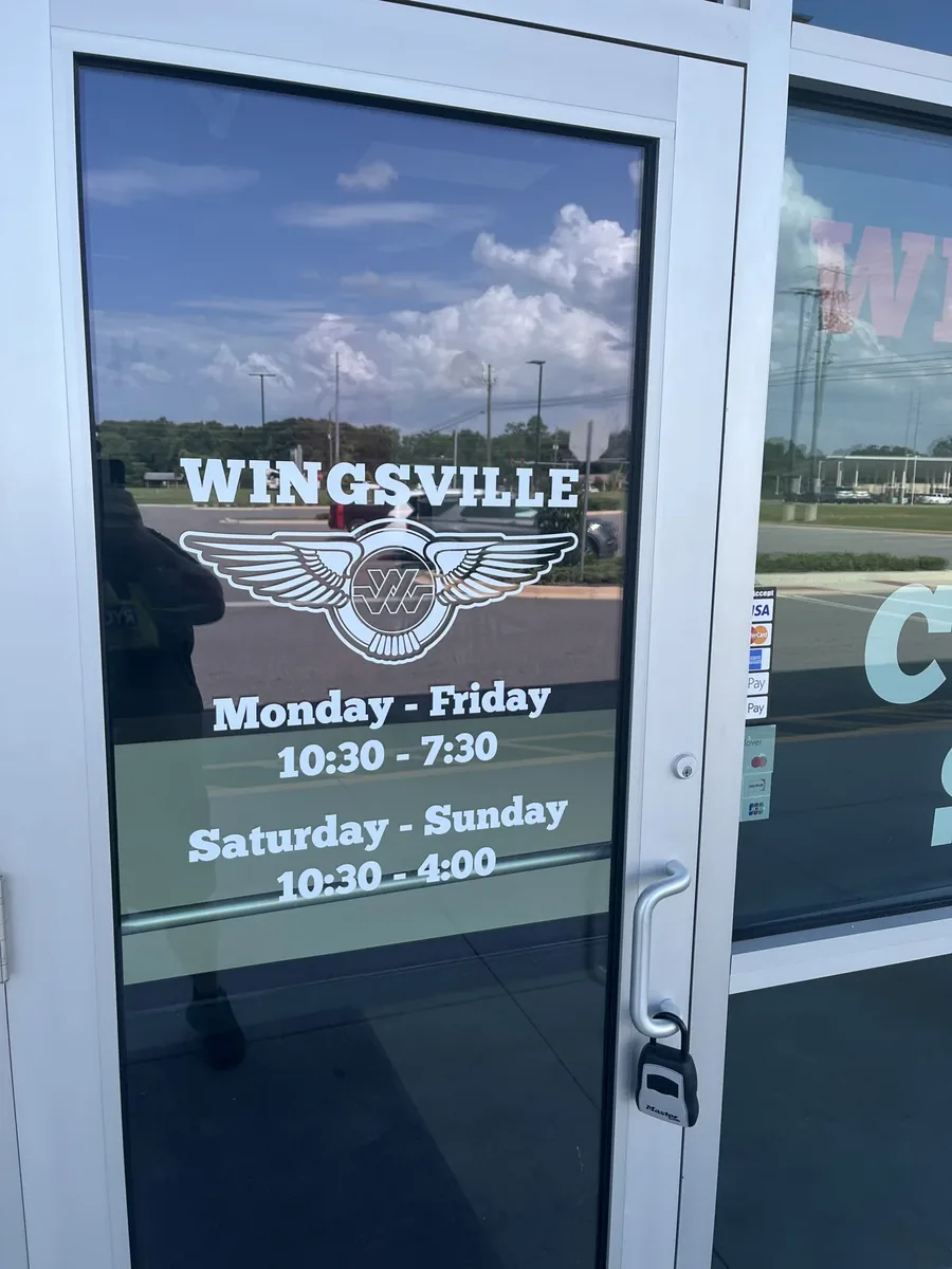 Wingsville winged logo and opening hours in white vinyl lettering on a glass door